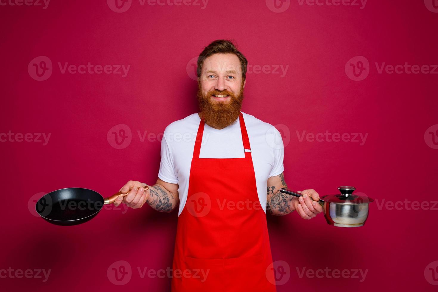 Happy chef with beard and red apron cooks with pan and pot photo