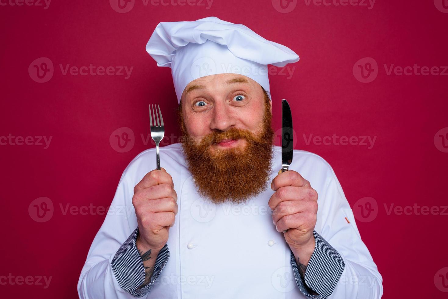 contento cocinero con barba y rojo delantal sostiene cuchillería en mano foto