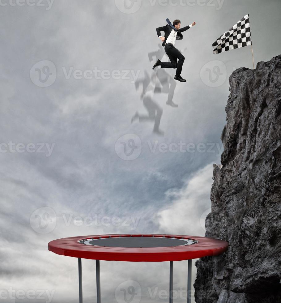 Businessman jumping on a trampoline to reach the flag. Achievement business goal and Difficult career concept photo