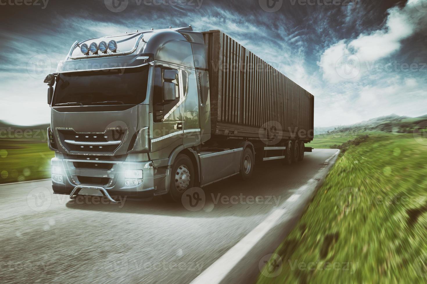 Grey truck moving fast on the road in a natural landscape with cloudy sky photo