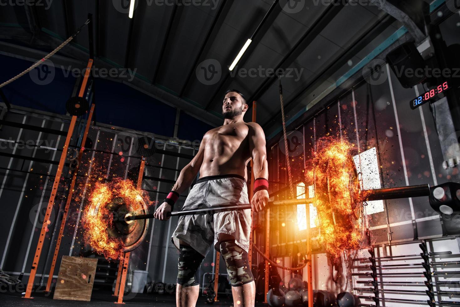 Athletic man works out at the gym with a fiery barbell photo