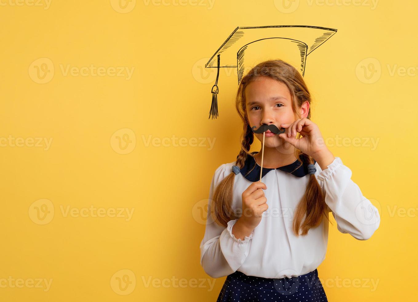 Young student acts like a graduate. Yellow studio background photo