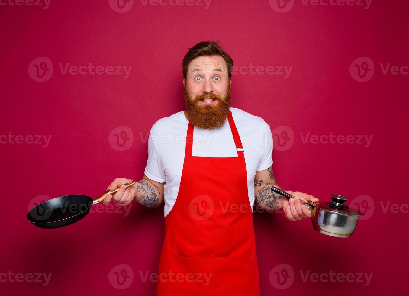 afraid chef with beard and red apron cooks with pan and pot photo