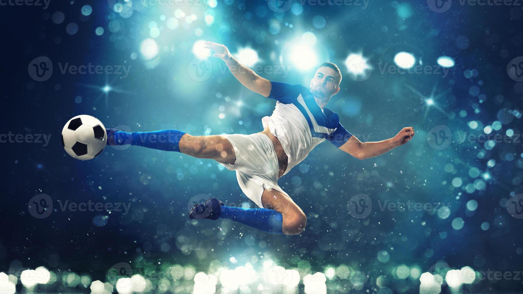 Soccer striker hits the ball with an acrobatic kick in the air on dark blue background photo