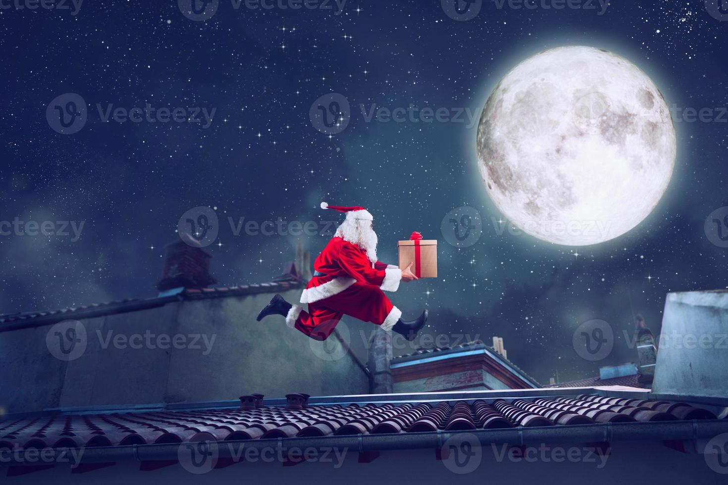 Santa Claus runs fast on a roof with a present photo