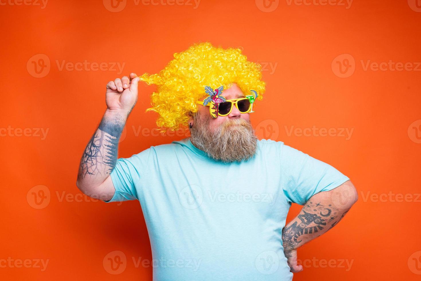 Fat happy man with beard, tattoos and sunglasses has fun with the yellow wig photo