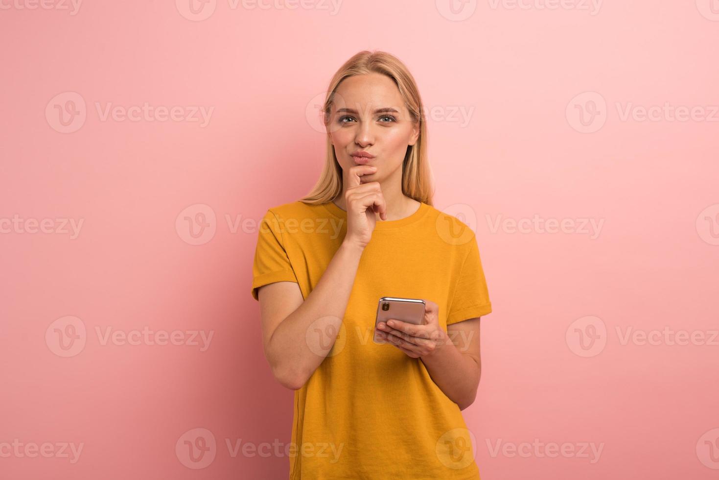 Blonde girl thinks about the right option. Yes or no. Confused and pensive expression. Pink background photo