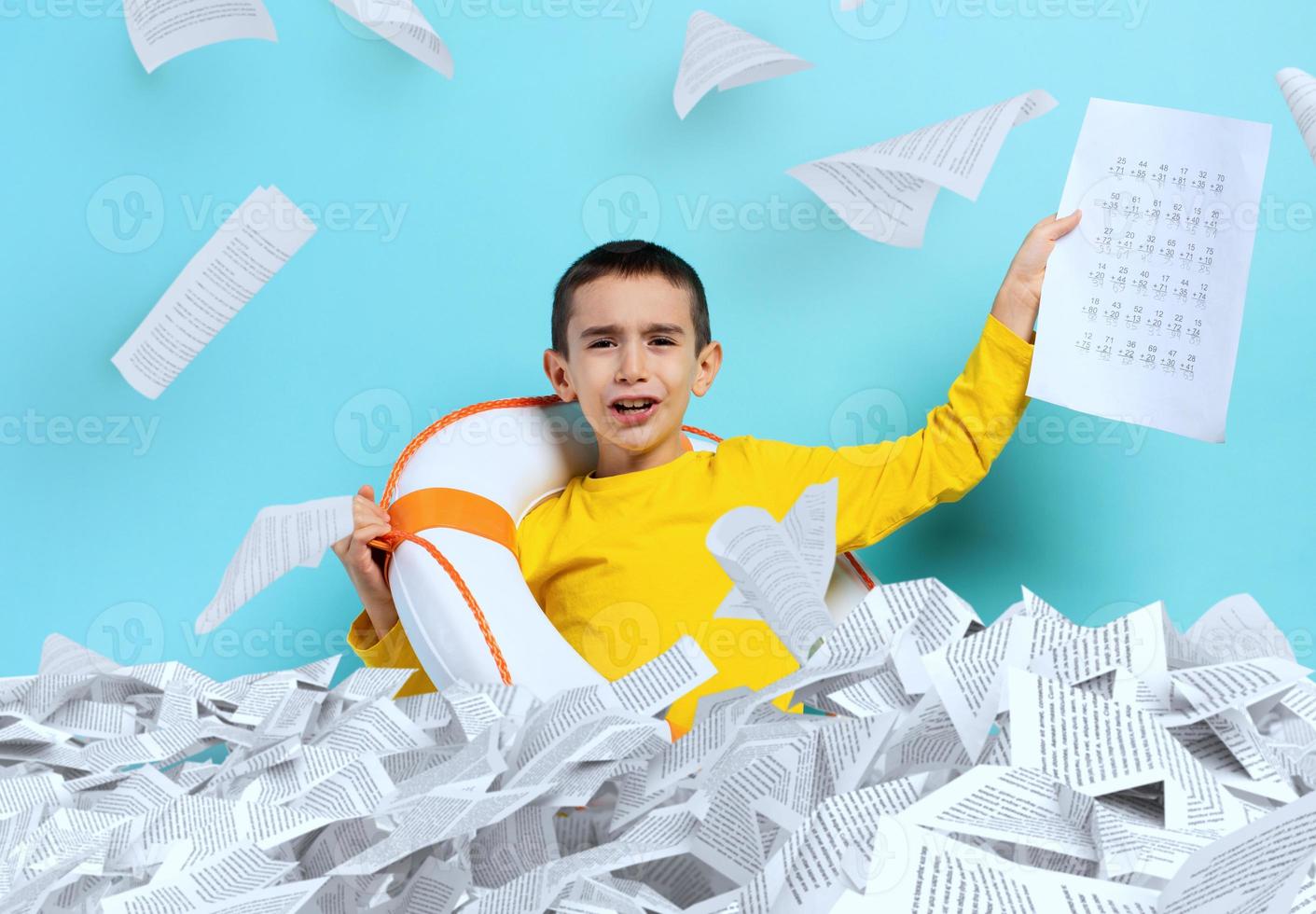 Young boy student is drowning in a sea of sheets of exercises. Cyan background photo