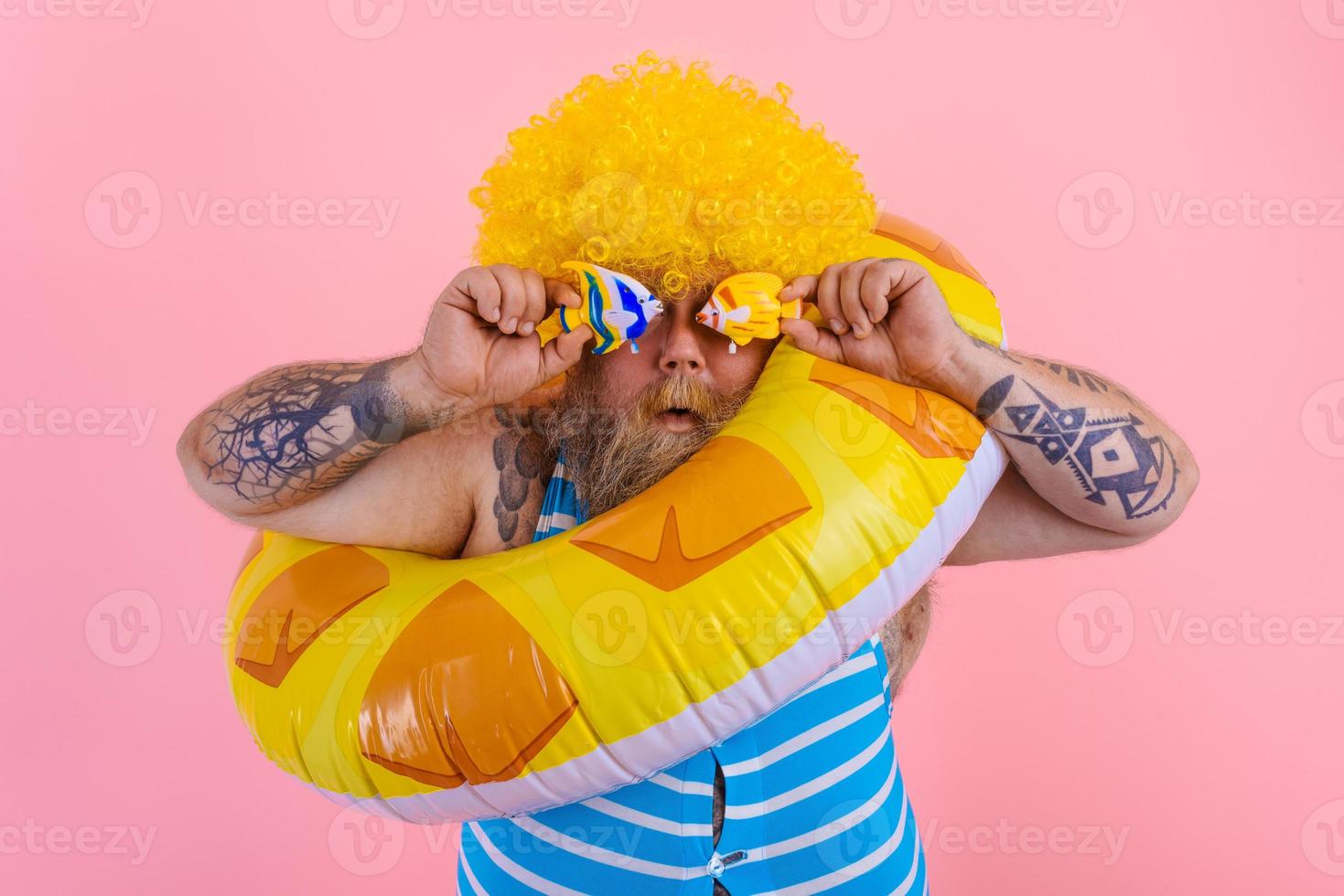Fat amazed man with wig in head is ready to swim with a donut lifesaver photo