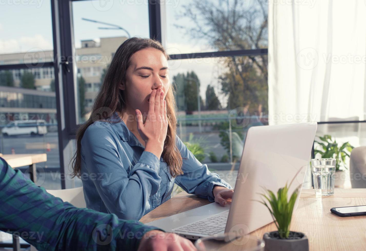 Tired girl yawns during the work with her laptop photo