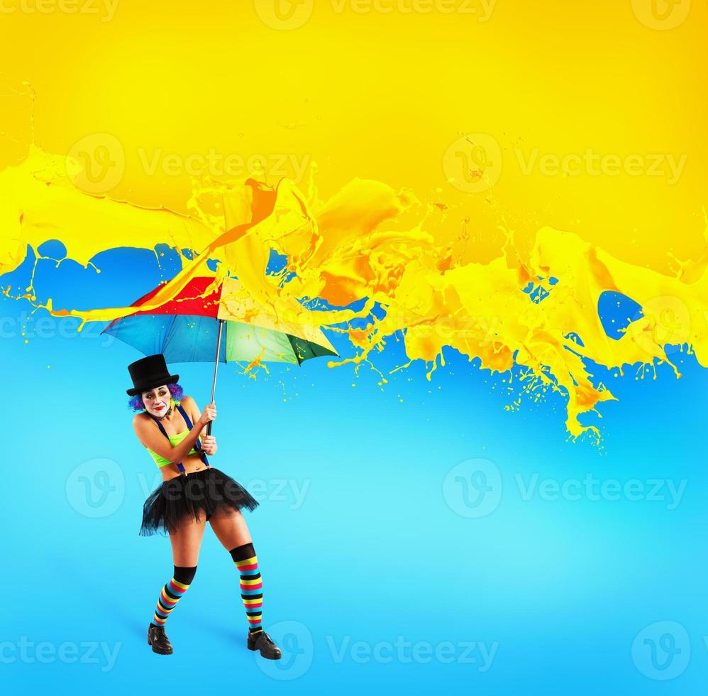 Clown with umbrella covers himself from yellow color drops photo