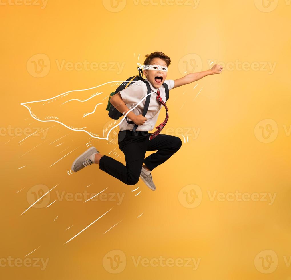 Young boy student jumps high like a super hero. Yellow background photo