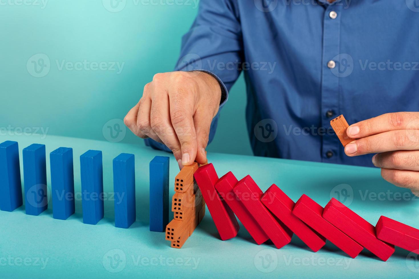 Businessman stops a chain fall like domino game. Concept of preventing crisis and failure in business. photo