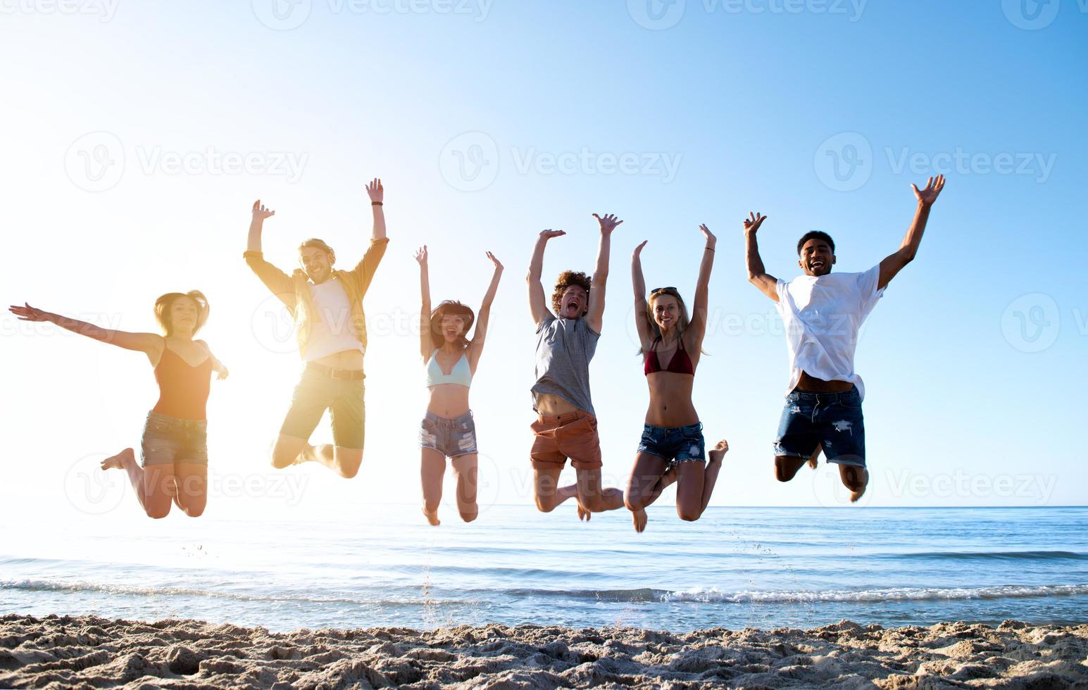Happy smiling friends jumping at the beach photo