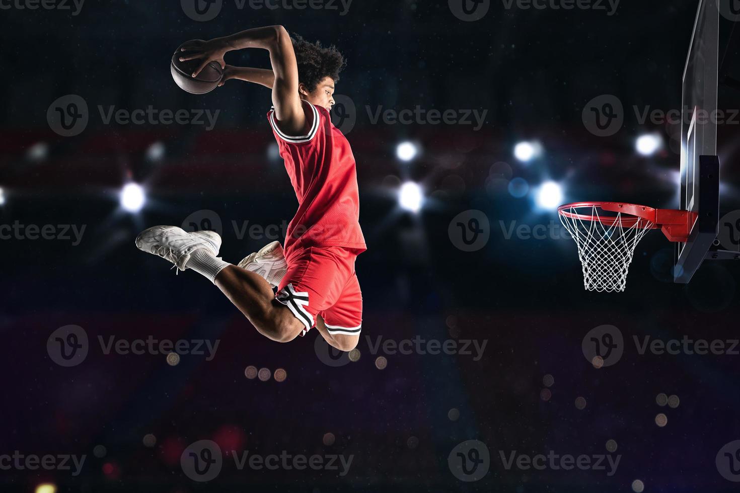 Basketball player in red uniform jumping high to make a slam dunk to the basket photo