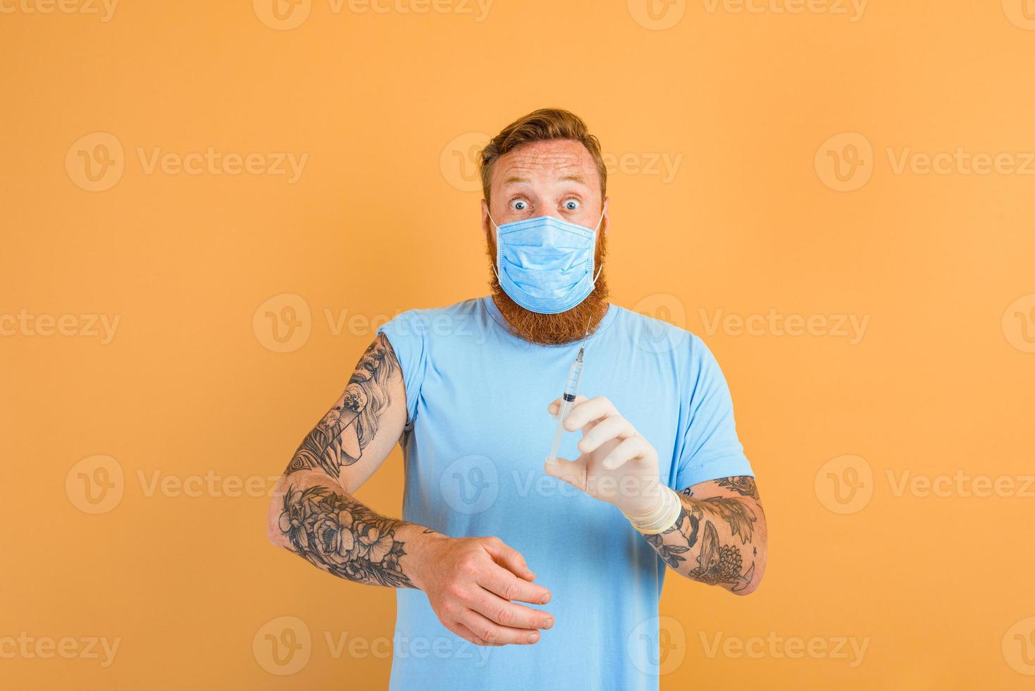 Afraid man with beard, tattoo and mask for covid-19 is ready for the virus vaccine photo