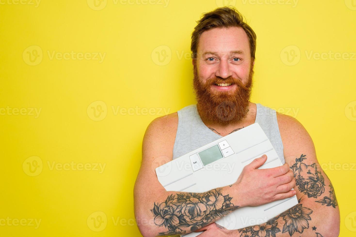 Happy man with beard and tattoos holds an electronic balance photo