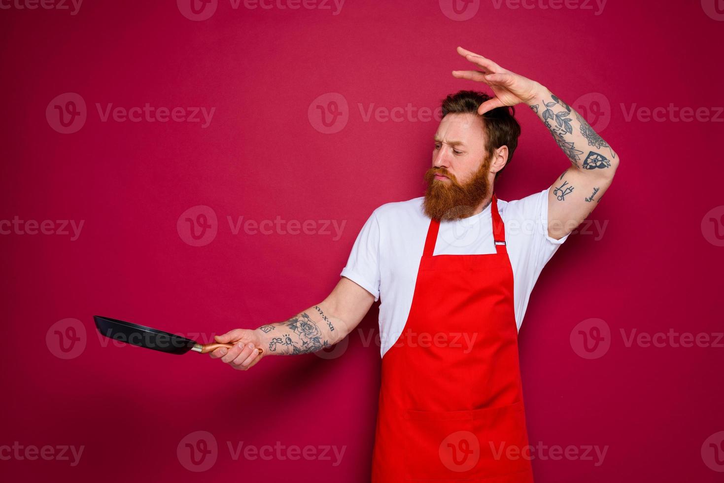 serious chef with beard and red apron cooks with pan photo