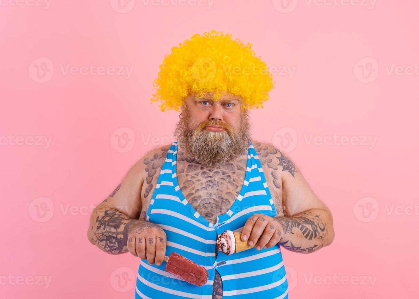 Fat man with beard and wig eats a popsicle and an icecream photo