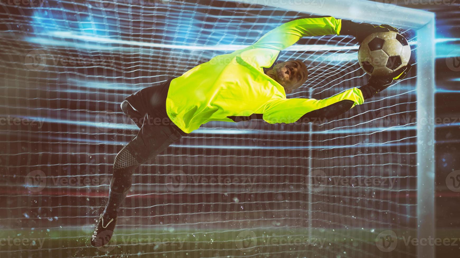Soccer goalkeeper, in fluorescent uniform, makes a save and avoids a goal during a night match photo