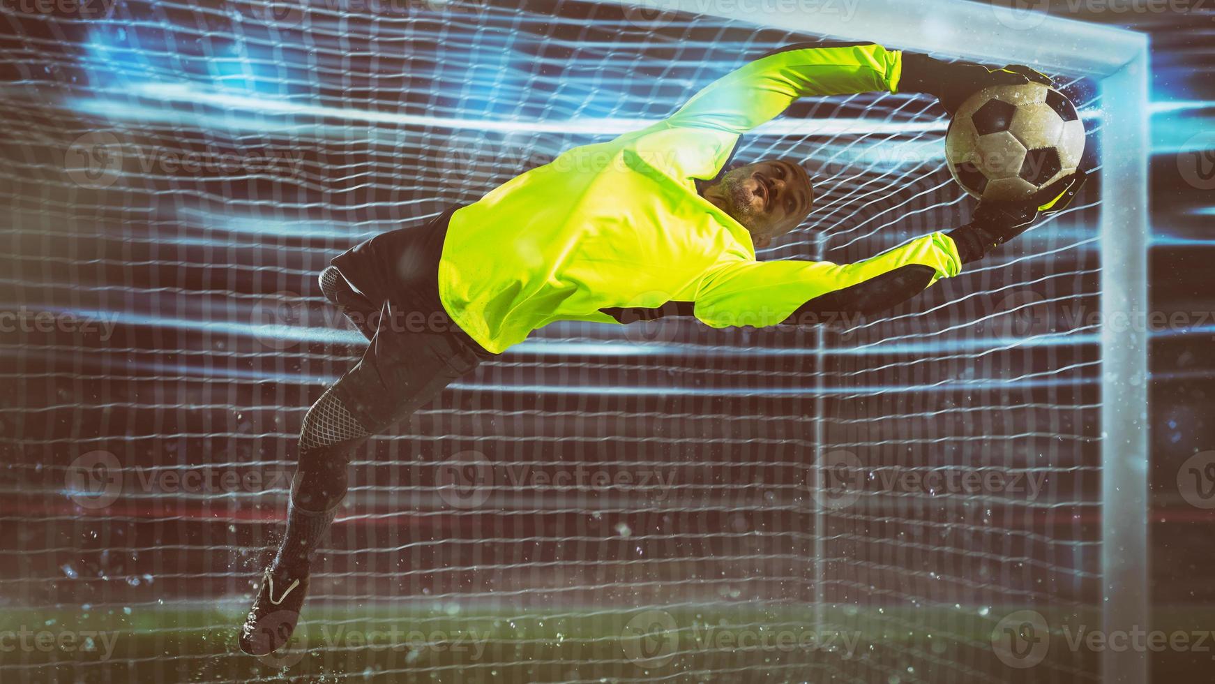 fútbol portero, en fluorescente uniforme, hace un salvar y evita un objetivo durante un noche partido foto