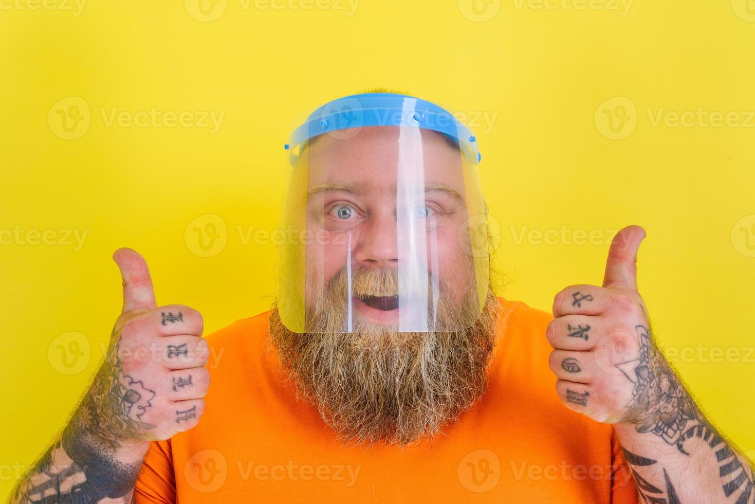 Happy man with beard and tattoos wears a protective face shield against covid-19 photo