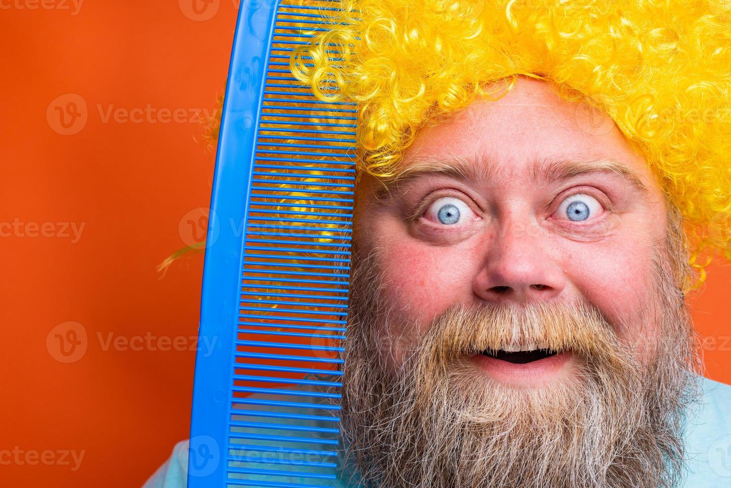 Fat amazed man with beard, tattoos and sunglasses combs himself with a giant comb photo