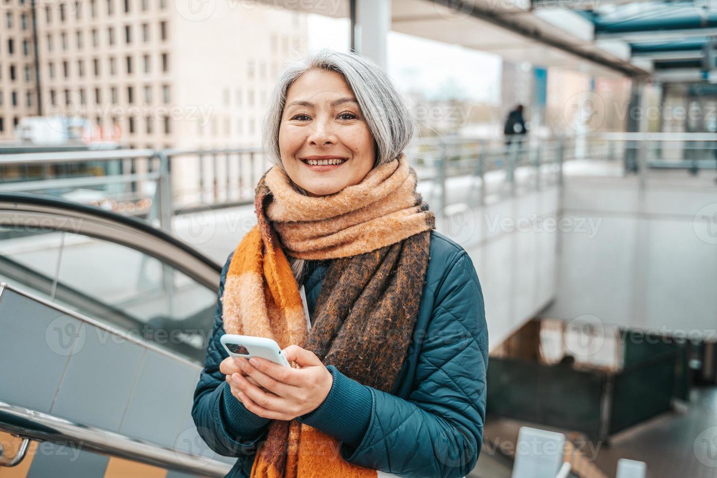 Senior woman send message with a mobile phone in a stransport station photo