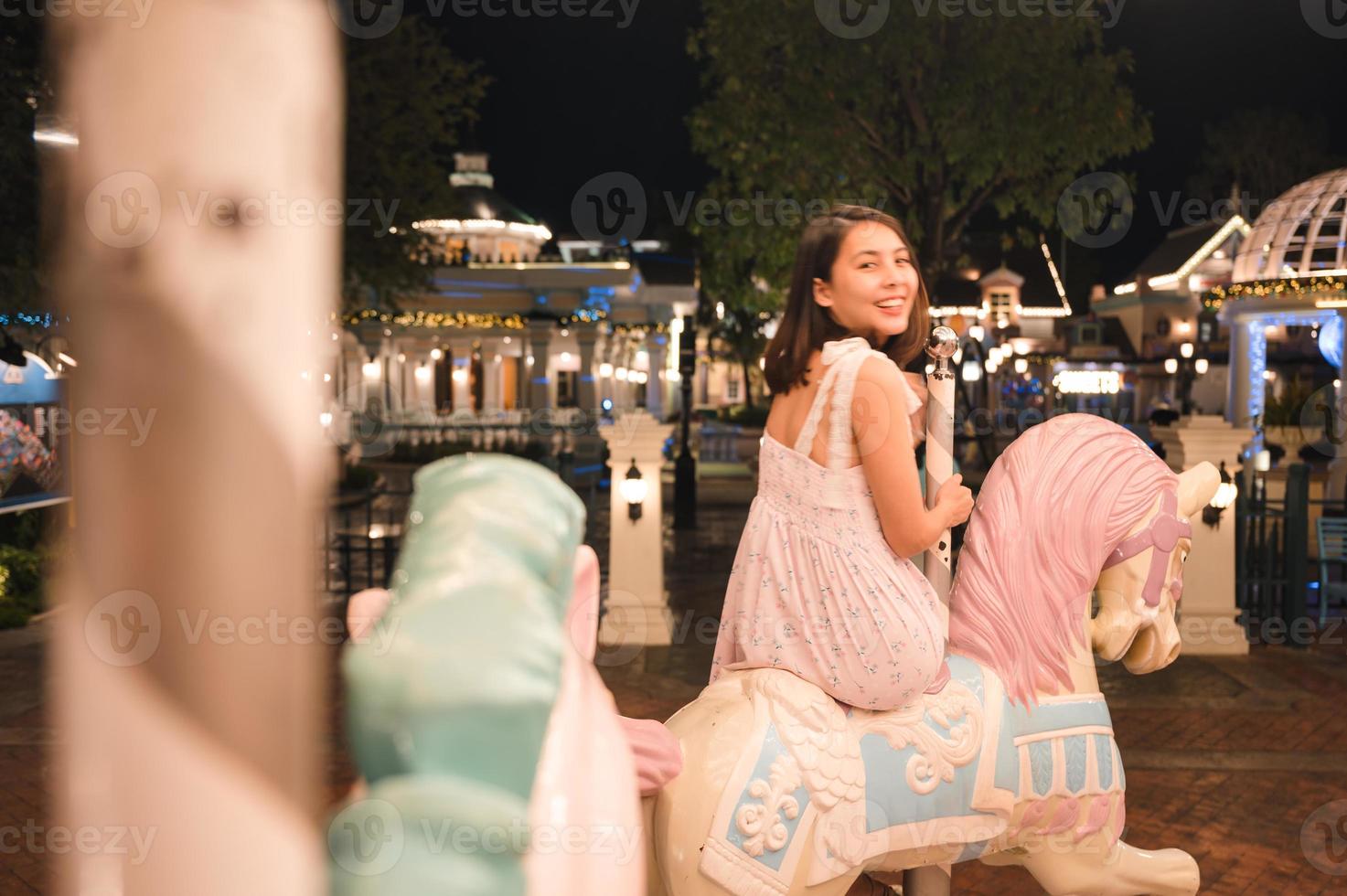 asiático mujer disfrutando en carrusel en diversión parque a noche foto