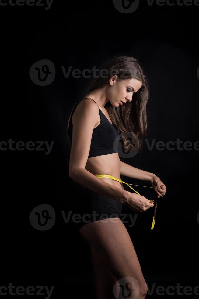 Retrato de una joven y bella mujer midiendo el tamaño de su figura con cinta métrica foto