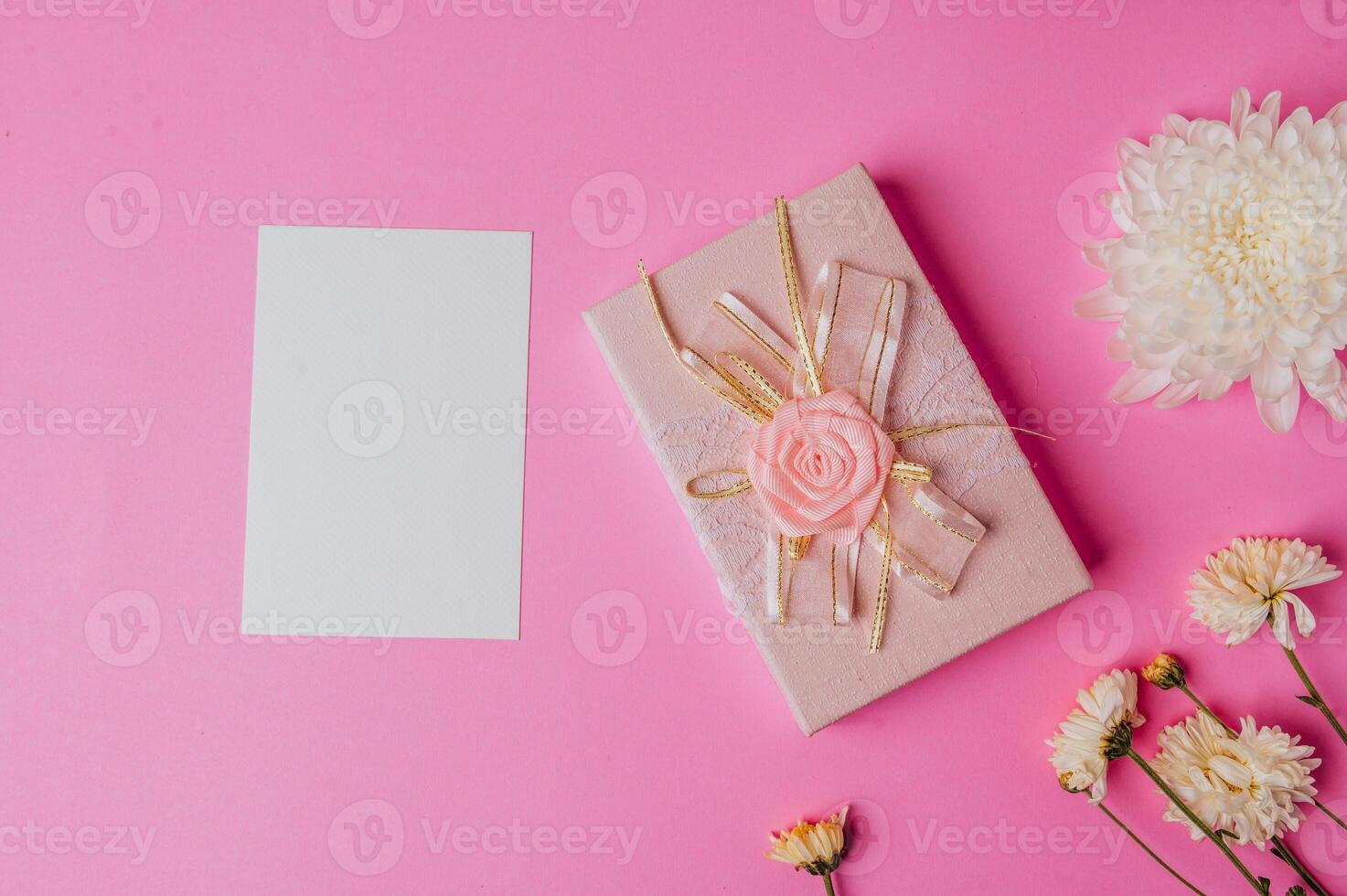 white paper and gift box on pink background decorated with flowers photo