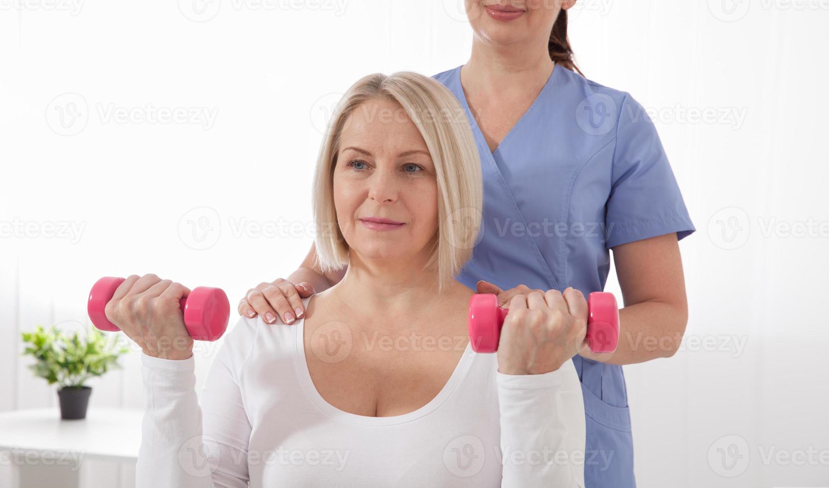A physiotherapist helps an older woman recover from an injury through exercise with dumbbells. photo