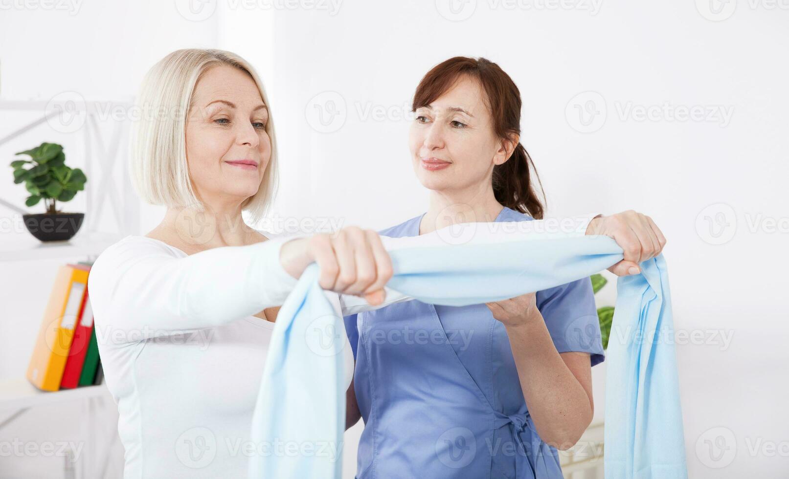 Physiotherapist and woman sitting on a bed exercising with a rubber tape photo