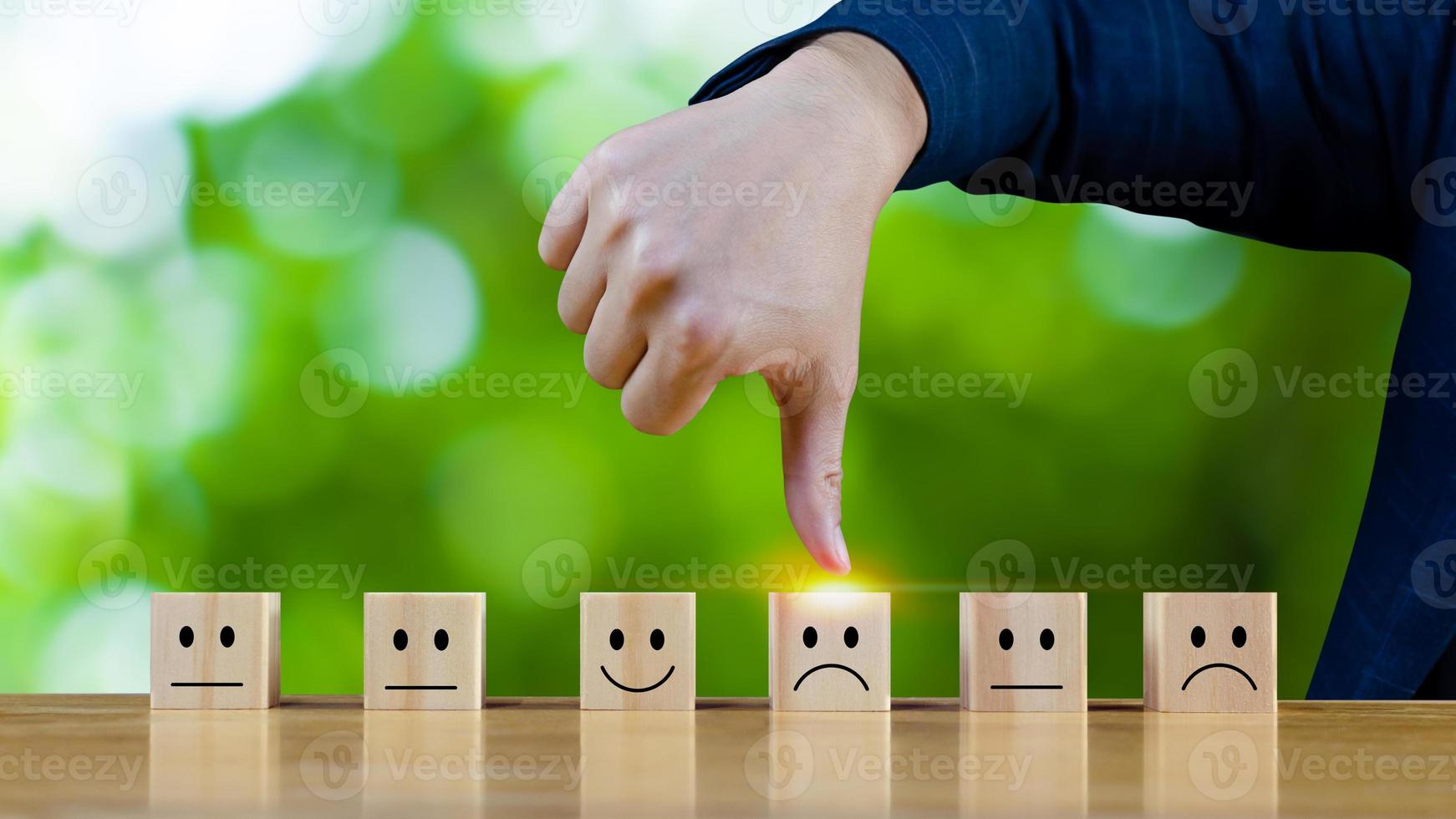 Customer service evaluation and satisfaction survey service rating concepts.Businessman hand thumbs down choose the wooden block with the Unhappy face smile face icon on wooden cube. photo