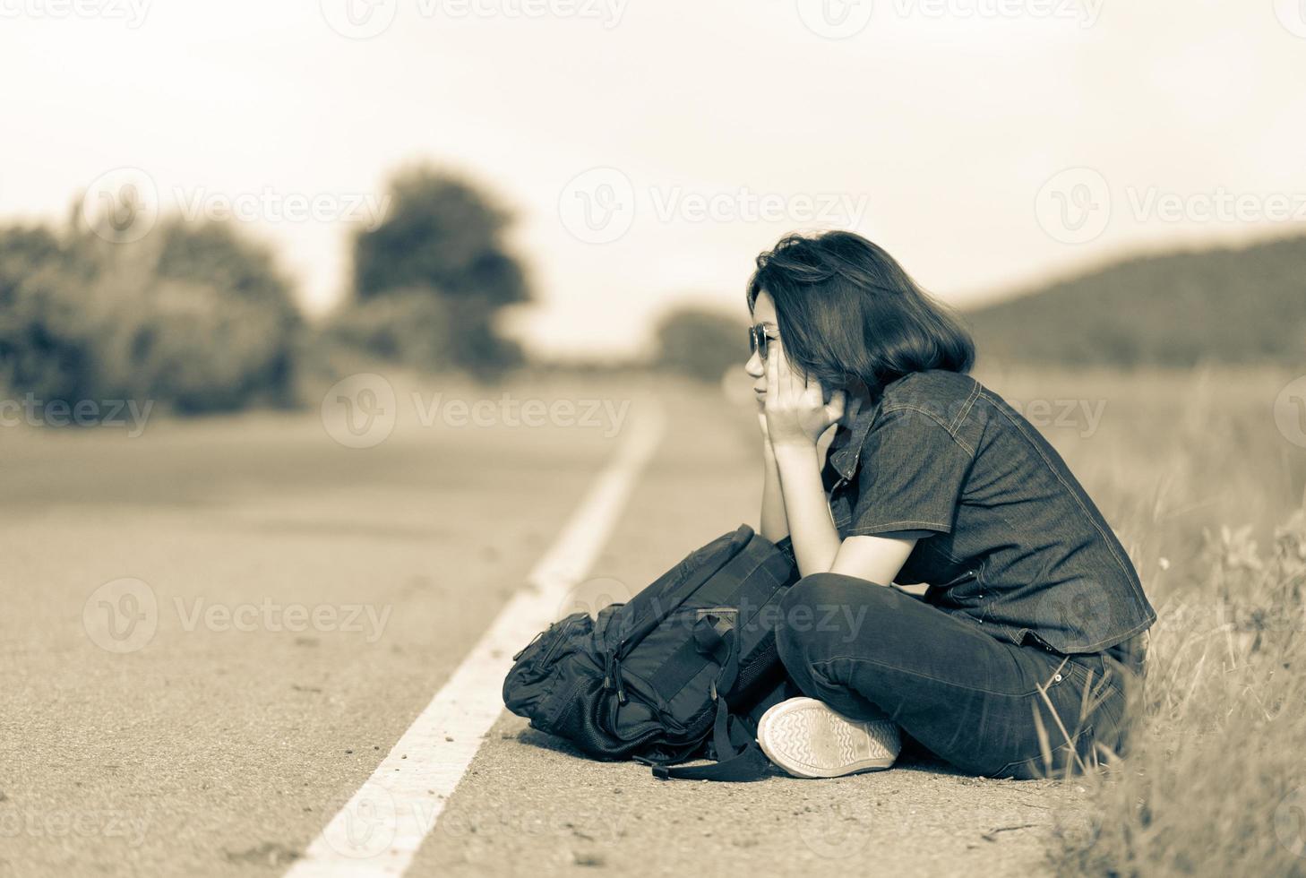 mujer sentada con mochila haciendo autostop a lo largo de una carretera en el campo foto