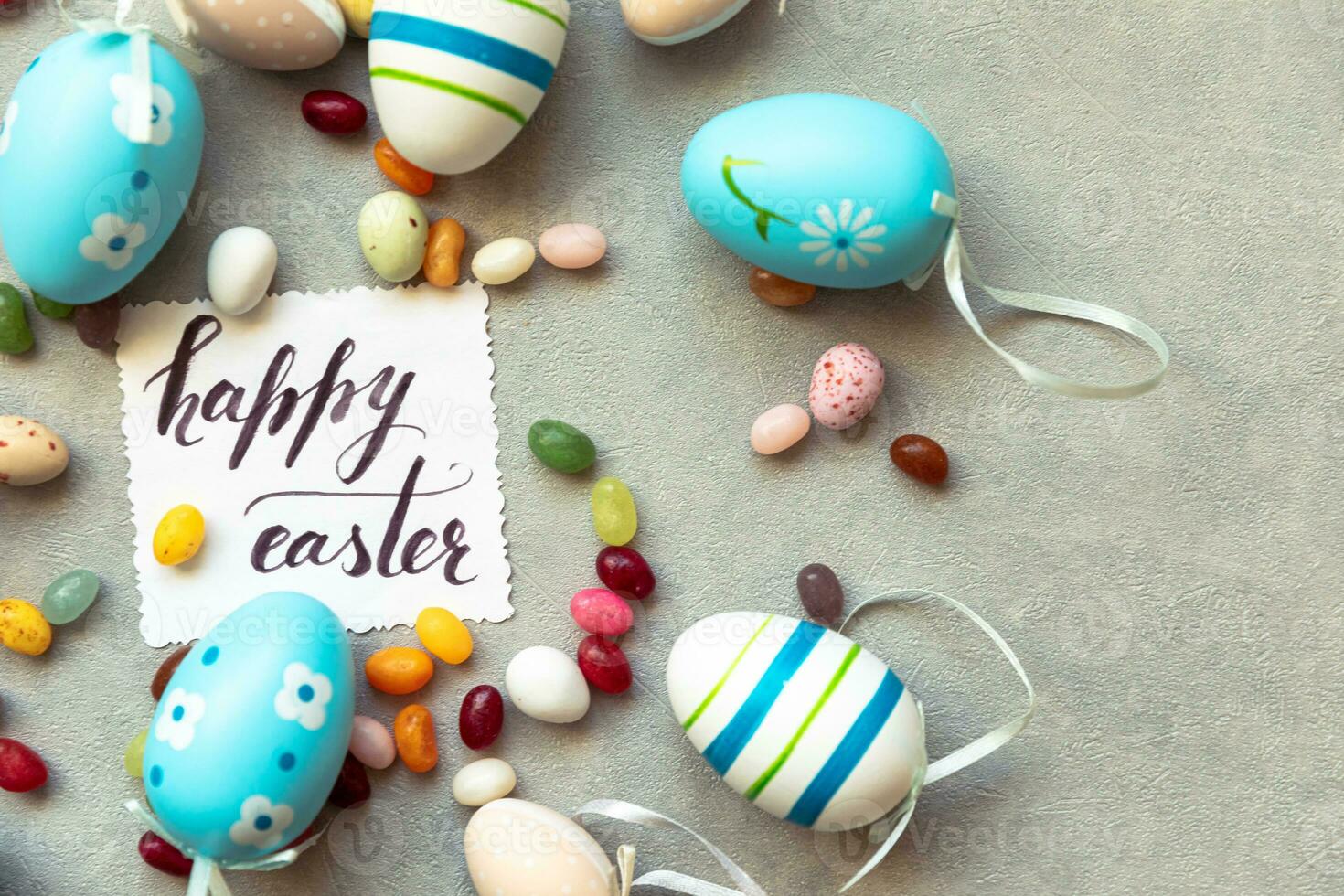 Happy Easter concept. Preparation for holiday. Easter eggs Inscription HAPPY EASTER letters candy chocolate eggs and jellybean sweets on concrete stone grey background. Flat lay top view copy space. photo