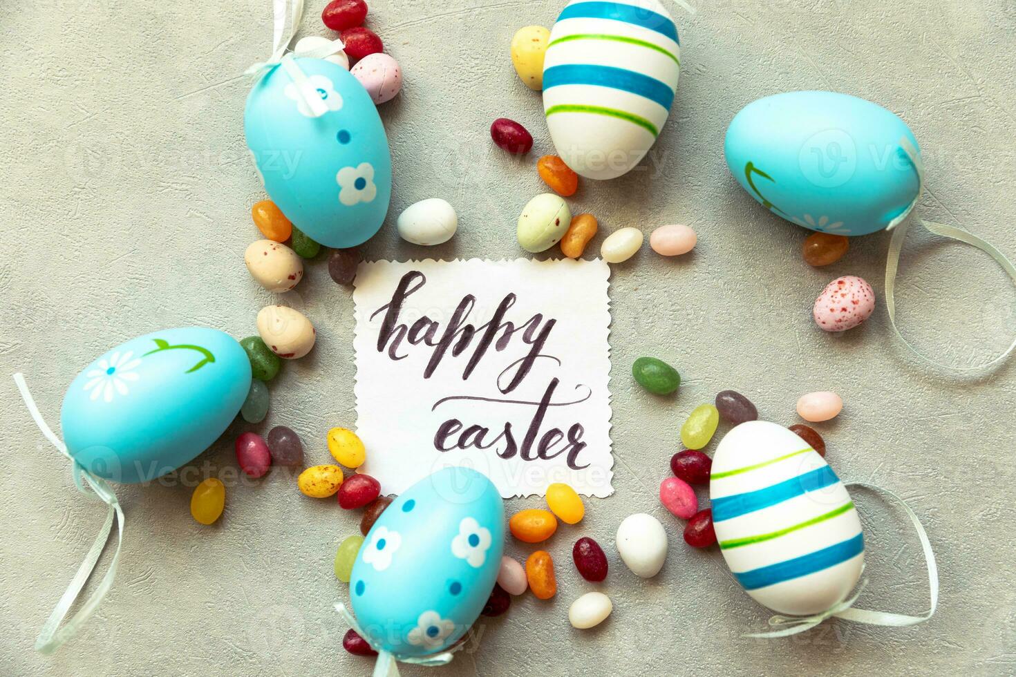 Happy Easter concept. Preparation for holiday. Easter eggs Inscription HAPPY EASTER letters candy chocolate eggs and jellybean sweets on concrete stone grey background. Flat lay top view copy space. photo