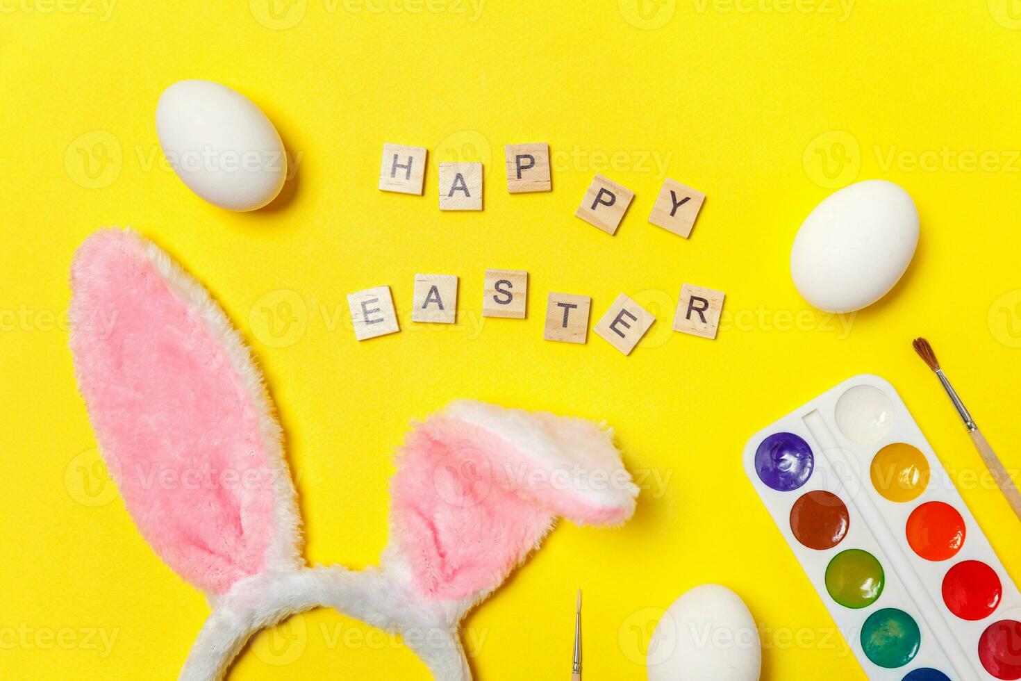 Inscription HAPPY EASTER letters eggs colorful paints and bunny ears isolated on trendy yellow background photo