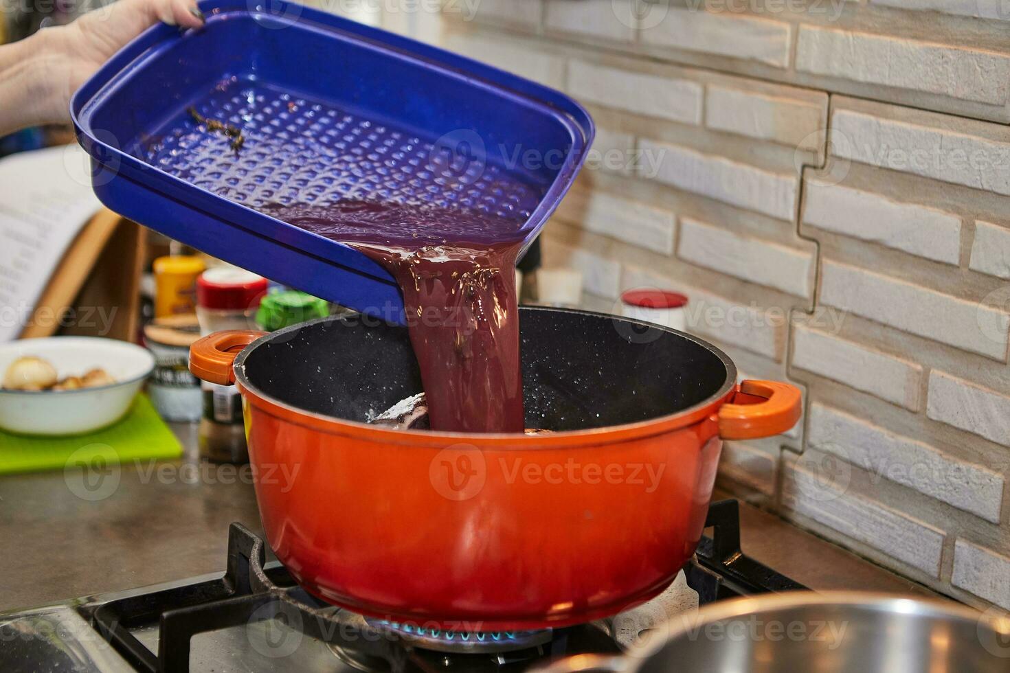 Chef pours the marinade into the chicken marinated in red wine with rosemary in pot on the gas stove photo