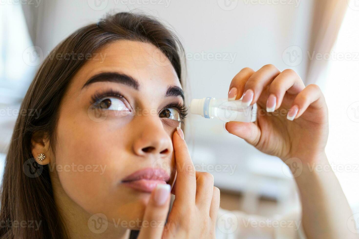 Photo of a woman using eye drop. Female dropping eye lubricant to treat