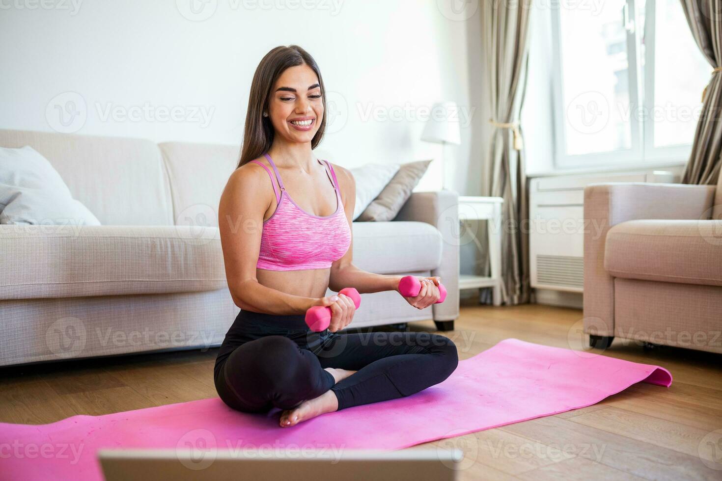 Young woman exercise with dumbbells at home and watching tutorial lesson on laptop computer. happy young female doing arm workout using dumbbells and looking at tutorial on her laptop photo