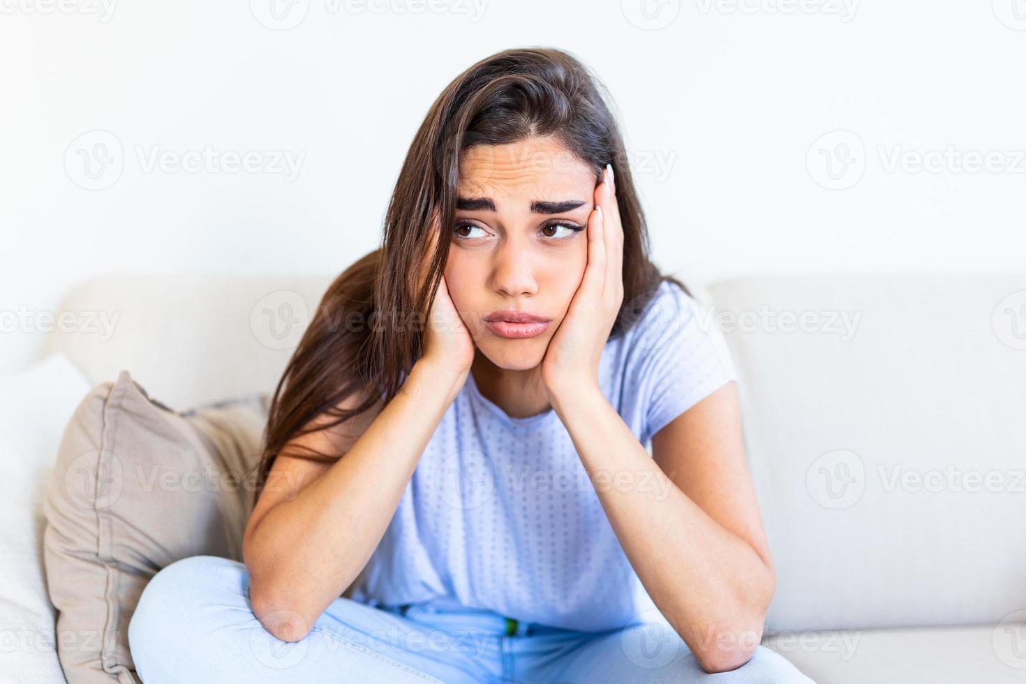 Young hopeless woman suffering from depression and anexiety. Having nervous breakdown. Sad and depressed young woman sitting on a couch in the living room at home photo