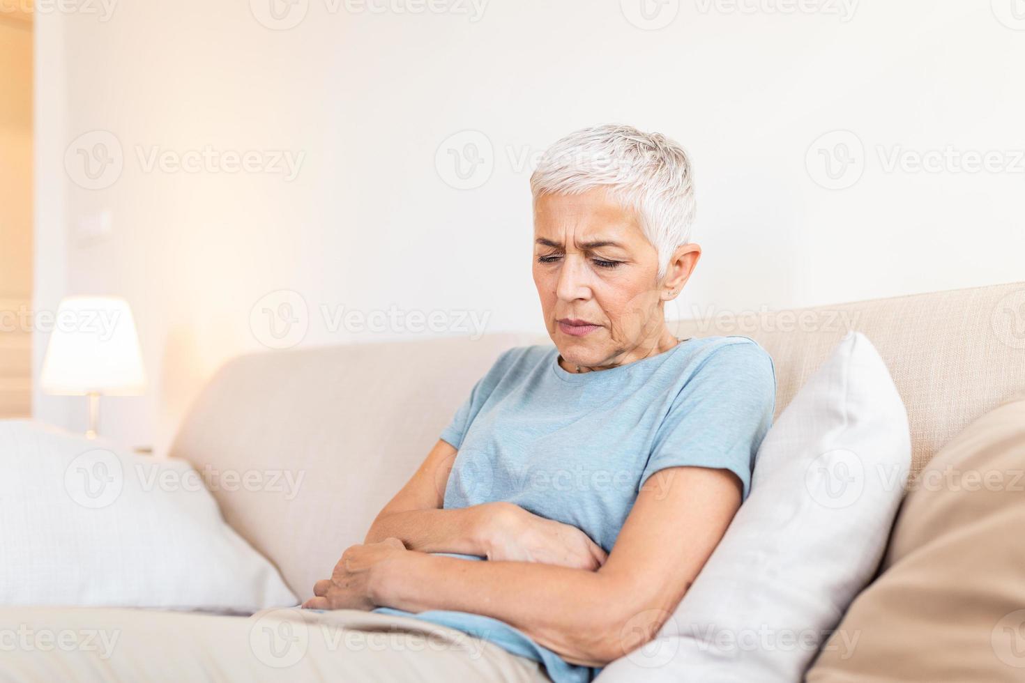 Old age, health problem and people concept - senior woman suffering from stomach ache at home. Senior woman suffering from stomach pain at home photo