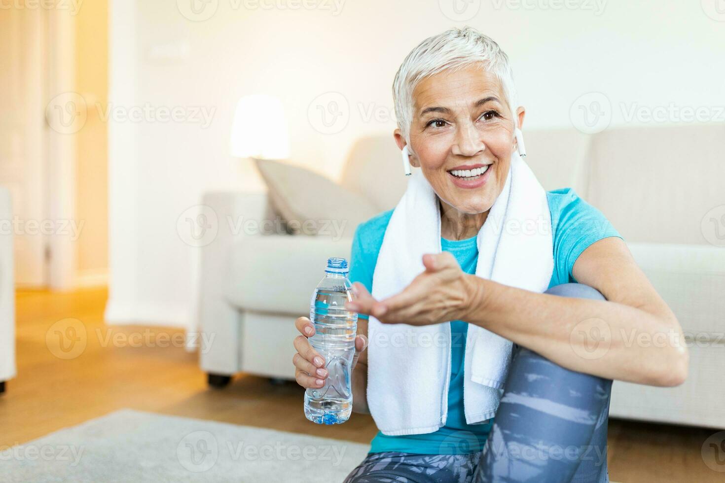 Senior woman with headphones while resting after workout. Holding a bottle of water. Athletic mature woman resting after a good workout session photo