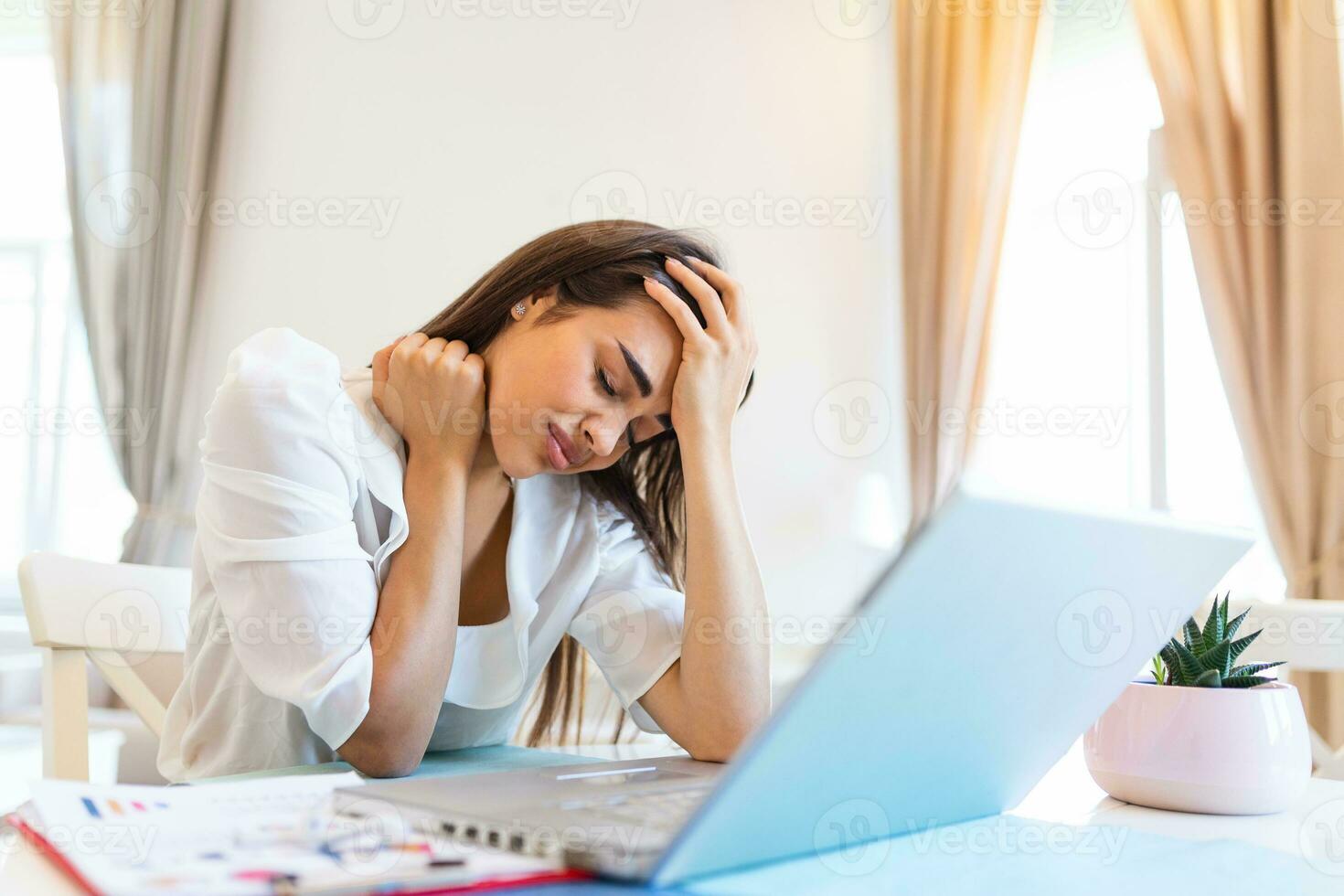 Young frustrated woman working from home office in front of laptop suffering from chronic daily headaches, treatment online, appointing to a medical consultation, electromagnetic radiation, sick pay photo