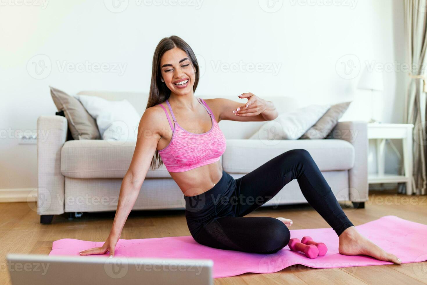 Gorgeous young woman on exercise mat at home and watching workout tutorial online on laptop. Video lesson. Young woman repeating exercises while watching online workout session photo