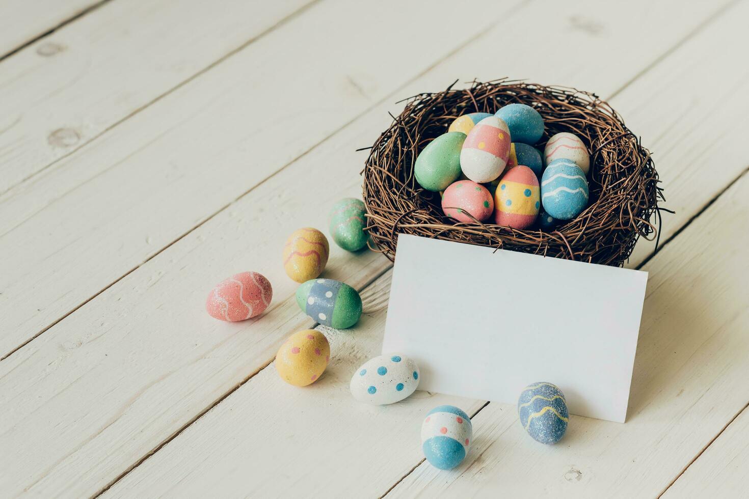 Colorful easter eggs in the nest and paper card on wood table background. photo