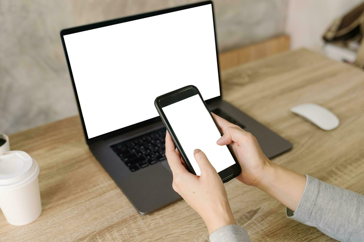 Asian woman holding phone and using computer laptop on wooden table photo