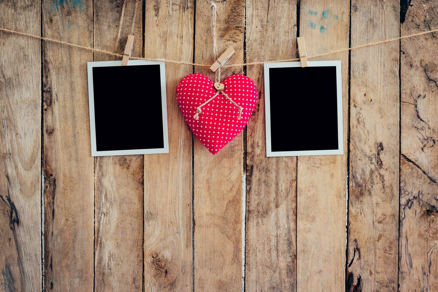 Red heart and two photo frame hanging on clothesline rope with wooden background.