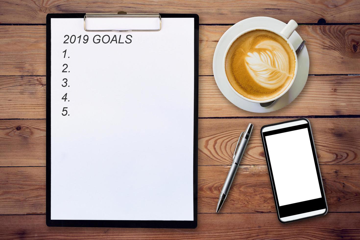 Top view of clipboard written Goals 2019 on wooden background with coffee cup, pen and mobile phone. photo
